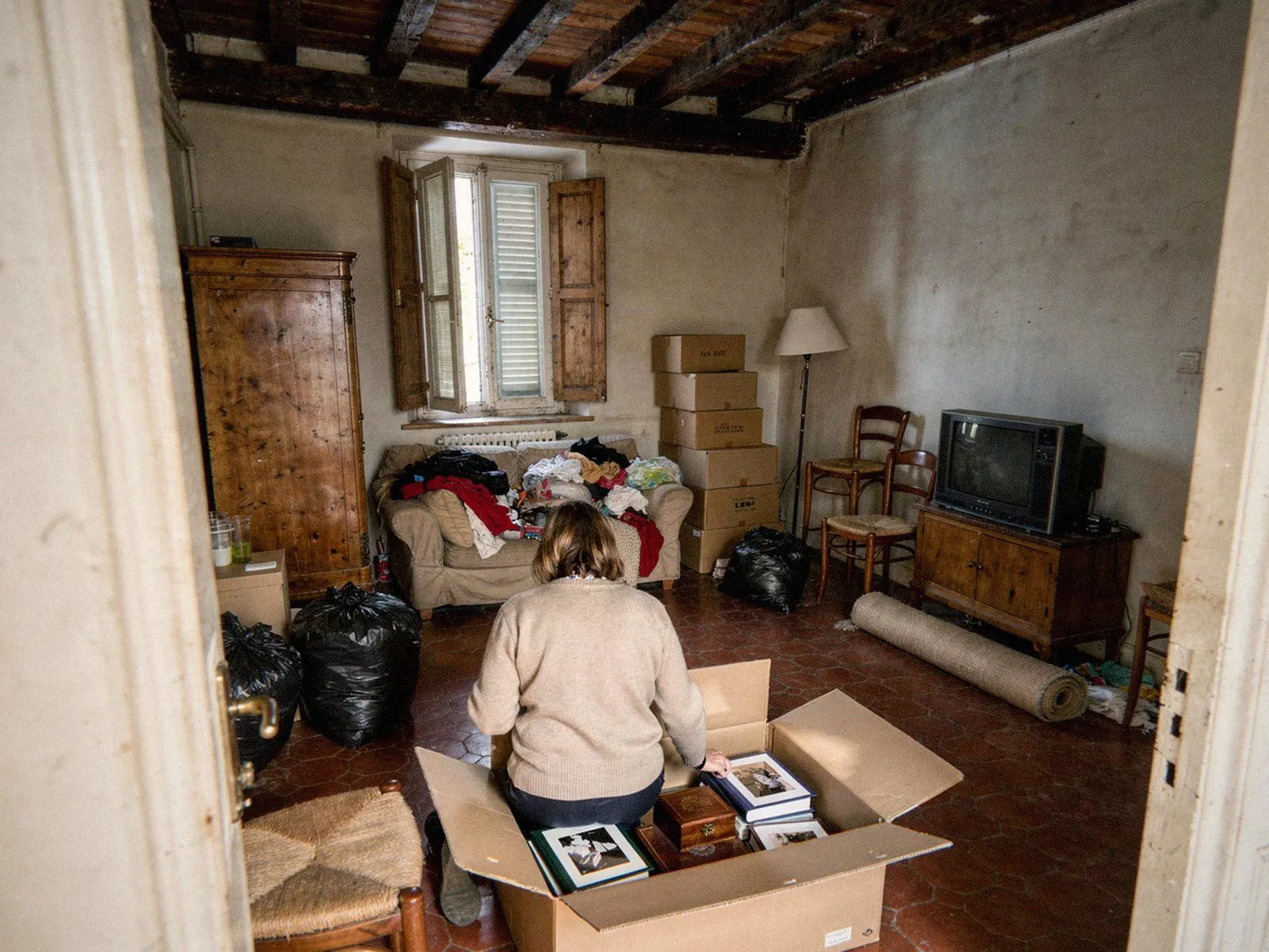 Une héritière range albums photo et souvenirs dans un carton avant le débarras d’un logement de famille à Lyon