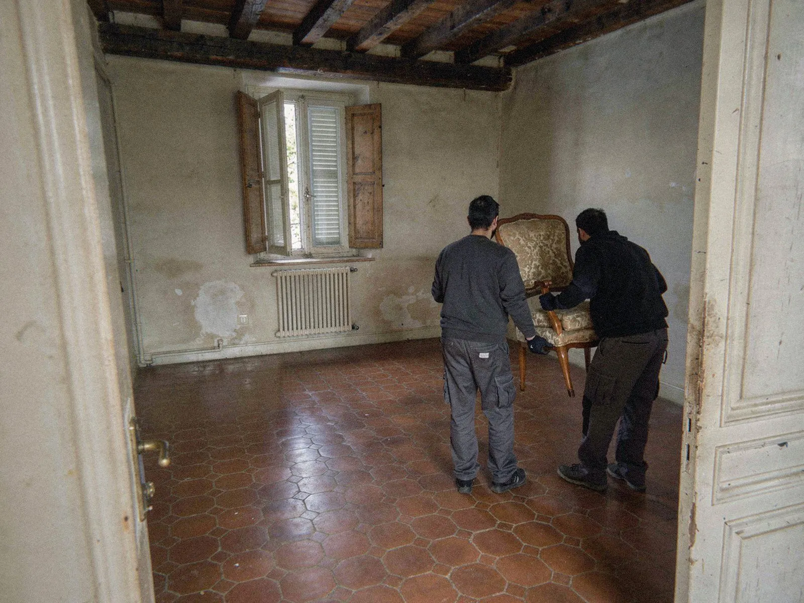 Deux intervenants d'OPM Débarras de dos emportent le dernier fauteuil du séjour presque vide à Lyon