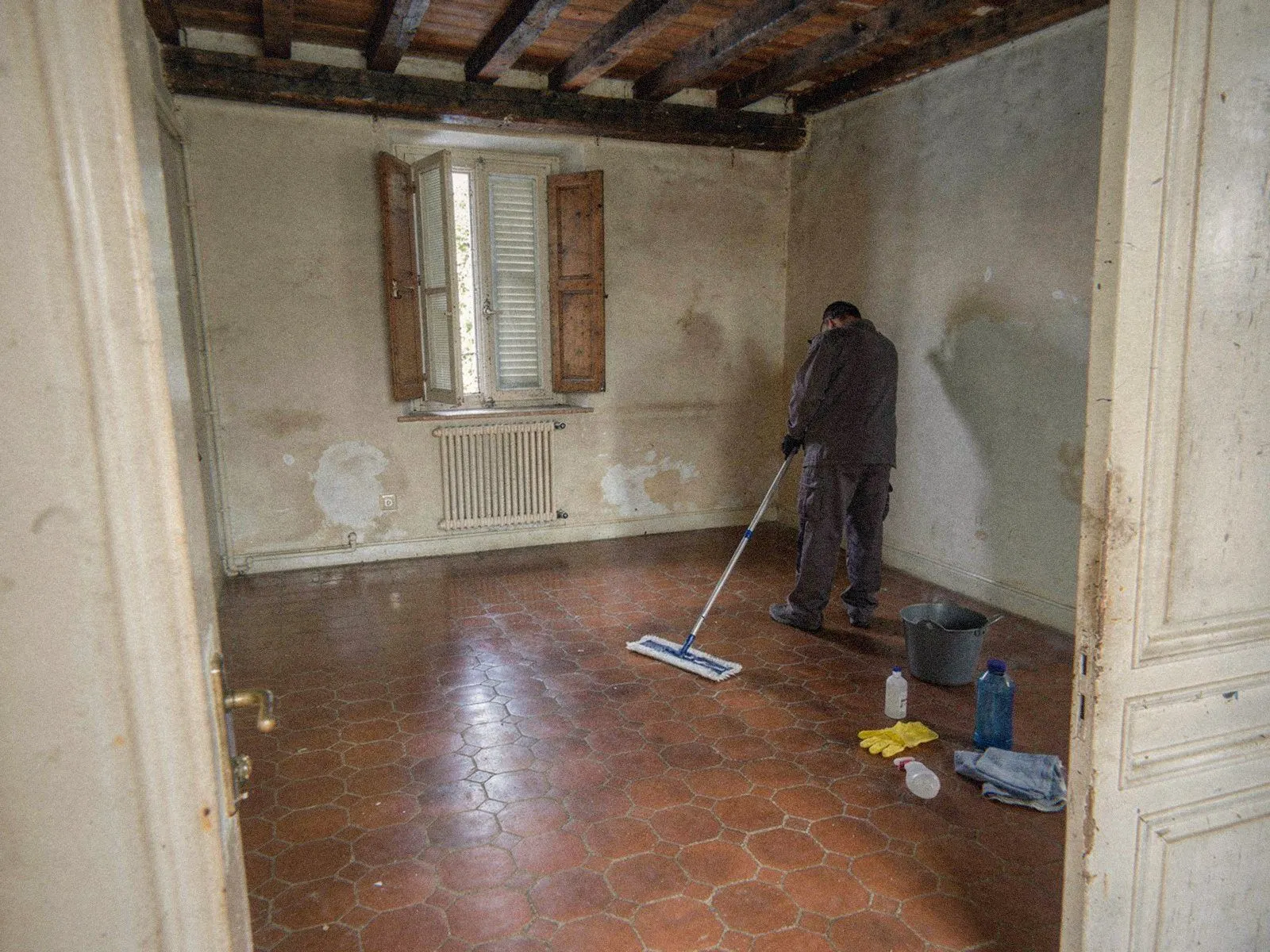 Intervenant d'OPM Débarras de dos lavant le sol du séjour vidé, seau et produits d'entretien à ses pieds, à Lyon