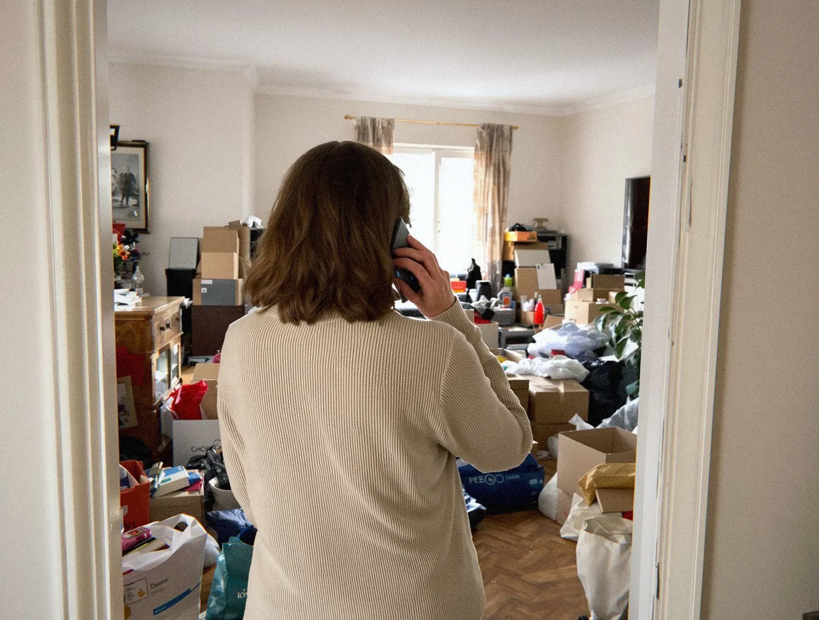 Une cliente de dos, téléphone à l'oreille, devant le séjour encombré qu'elle veut faire débarrasser à Lyon