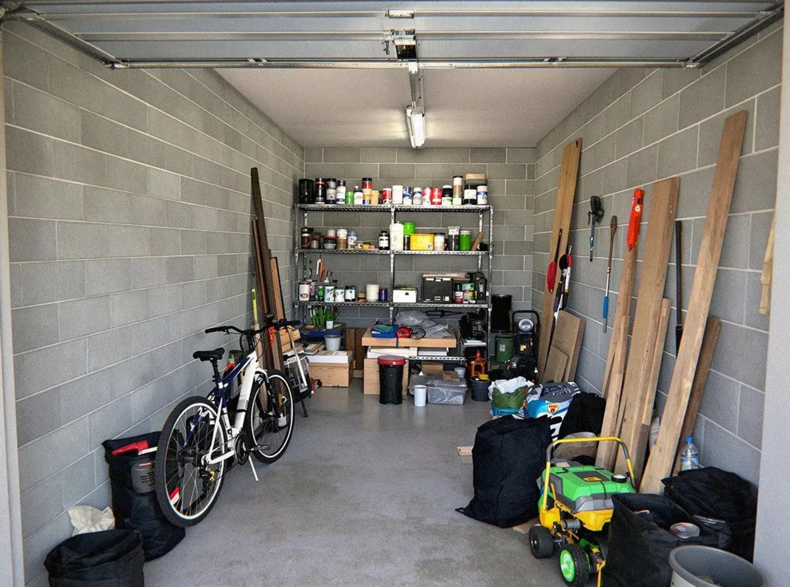 Garage en parpaings encombré d'outils, de planches et de sacs, photographié avant le débarras